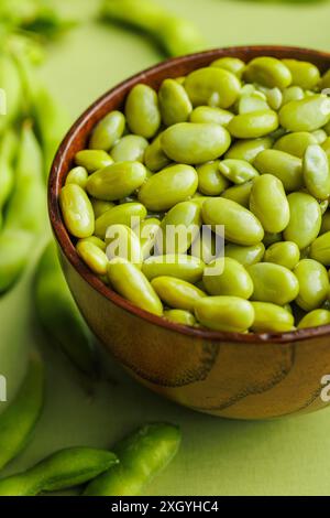 Cialde di edamame verdi. Semi di soia freschi nel recipiente su un tavolo verde. Foto Stock