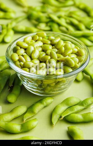 Cialde di edamame verdi. Semi di soia freschi nel recipiente su un tavolo verde. Foto Stock