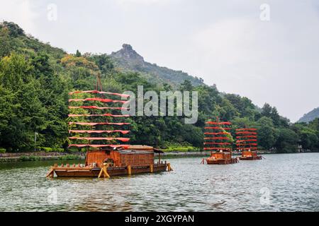 Incredibili navi in legno decorate con bandiere rosse e parcheggiate sul lago tra boschi verdi a Guilin, Cina. Guilin è una popolare destinazione turistica dell'Asia. Foto Stock