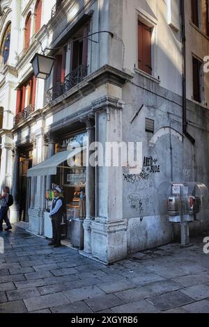 Gelateria ai margini di Piazza San Marco 'americano' con un giovane uomo a maniche bianche, gilet scuro e cravatta davanti in attesa di servire i clienti Foto Stock