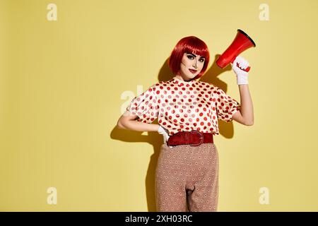 Una bella donna rossa con trucco pop art acconcia i suoi capelli rossi utilizzando un asciugacapelli retrò rosso e bianco su sfondo giallo. Foto Stock