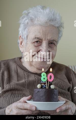 Una bella donna anziana che tiene la sua torta di compleanno per ottant'anni Foto Stock