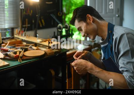 Abile lavoratore di pelli che cucisce, crea prodotti in pelle naturale nell'officina locale Foto Stock