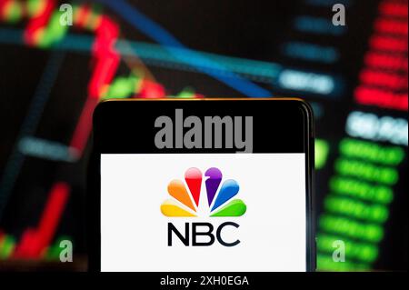 In questa illustrazione fotografica, il logo della rete televisiva di trasmissione commerciale in lingua inglese americana National Broadcasting Company (NBC) è stato visualizzato su uno smartphone con un grafico dell'indice di borsa economica sullo sfondo. Foto Stock
