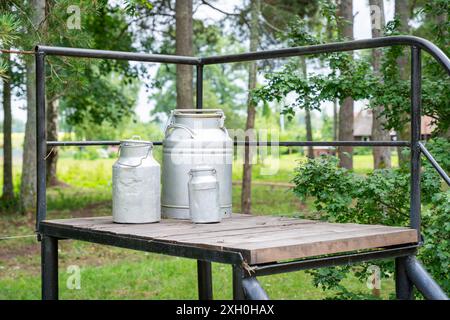 Il latte si trova su una piattaforma di legno ai lati di una strada di campagna. Il tradizionale supporto per la raccolta del latte viene mantenuto per scopi decorativi. Foto Stock