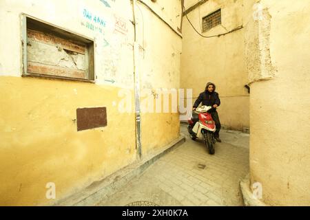 Un giovane cammina spingendo il suo scooter attraverso le stradine della medina di Fez in Marocco, Nord Africa. Foto Stock