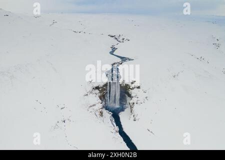 Vista aerea della cascata Skogafoss in Islanda durante l'inverno, circondata da paesaggi innevati con i visitatori alla base. Foto Stock