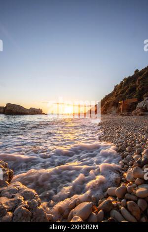 Baia nascosta sul Mediterraneo all'alba. Guarda la piccola spiaggia di sabbia e ciottoli, la spiaggia è bagnata dai colori caldi dell'alba nel Foto Stock