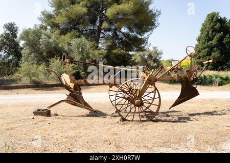 Un aratro arrugginito d'epoca con vecchie ruote in legno in un ambiente rurale rustico Foto Stock