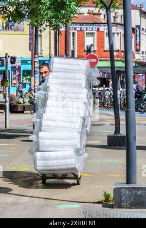 Carrello di trasporto uomo (nascosto) carico di molti pacchi di vassoi di plastica - Montreuil 93100, Senna-Saint-Denis, Francia. Foto Stock