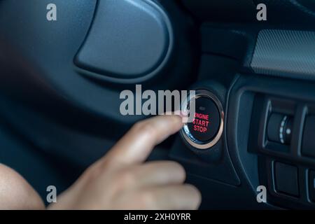 La mano di una giovane donna sta premendo il pulsante START in un'auto Foto Stock