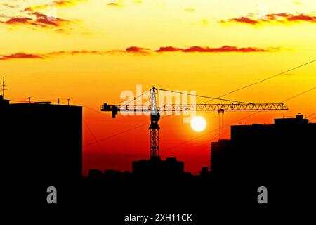 Silhouette di case e gru da cantiere contro il sole tramontato, skyline della città al tramonto Foto Stock