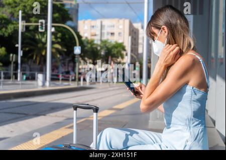 Spostarsi in città durante la nuova normalità. Donna con maschera protettiva contro l'epidemia di Coronavirus in attesa alla stazione del tram. Foto di alta qualità Foto Stock