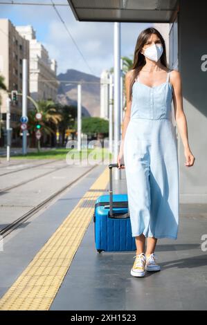 Spostarsi in città durante la nuova normalità. Donna con maschera protettiva contro l'epidemia di Coronavirus in attesa alla stazione del tram. Foto di alta qualità Foto Stock