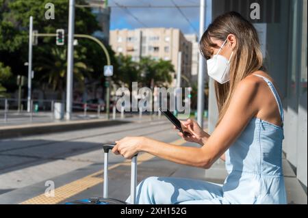 Spostarsi in città durante la nuova normalità. Donna con maschera protettiva contro l'epidemia di Coronavirus in attesa alla stazione del tram. Foto di alta qualità Foto Stock