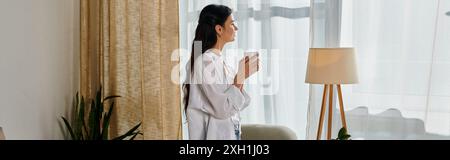 Ambiente informale da ufficio domestico; donna che si gusta un caffè vicino alla finestra. Foto Stock