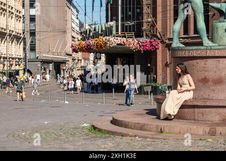 Giovane donna in abiti estivi seduta su un piedistallo scultoreo nella zona pedonale Aleksanterinkatu nel quartiere Kluuvi di Helsinki, Finlandia Foto Stock