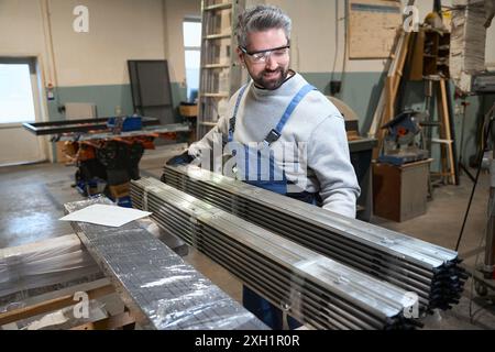 Il caposquadra in un'officina esamina una pila di profili in alluminio Foto Stock