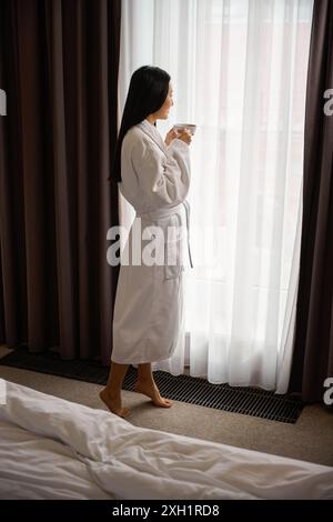Rilassata donna asiatica in accappatoio bianco godendosi la calma mattinata Foto Stock