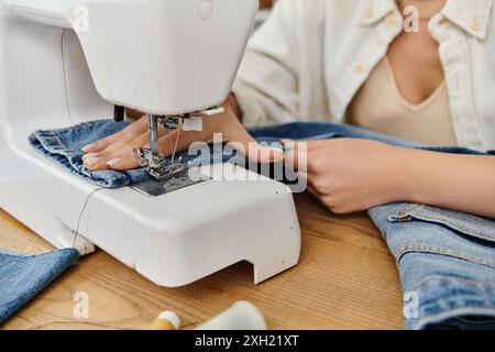 Una giovane donna con un abbigliamento casual che crea jeans upcycled su una macchina da cucire. Foto Stock