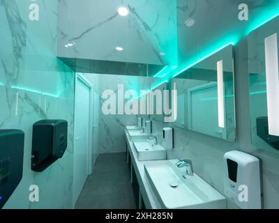 Bagno contemporaneo con pareti in marmo, lavandini multipli, specchi e illuminazione al neon. Il design enfatizza la pulizia e la raffinatezza, creando un ambiente elegante e igienico. Foto Stock