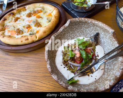Primo piano di una deliziosa pizza e un piatto di verdure arrosto servito su un tavolo di legno. Perfetto per gli amanti del cibo e della cucina. Foto Stock