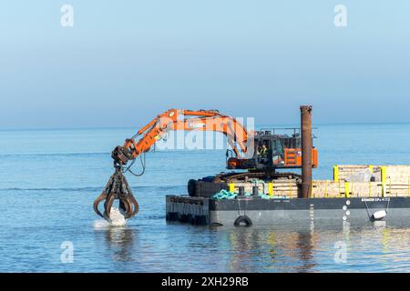 Lavori di protezione contro l’erosione costiera con macchinari provenienti da una chiatta in mare, Cromer, Norfolk, Inghilterra, Regno Unito, Europa Foto Stock