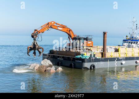 Lavori di protezione contro l’erosione costiera con macchinari provenienti da una chiatta in mare, Cromer, Norfolk, Inghilterra, Regno Unito, Europa Foto Stock