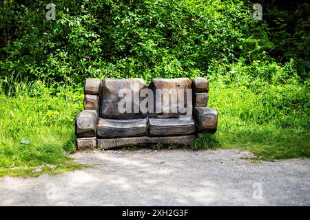 Panca rustica in legno intagliata per assomigliare ad un accogliente divano annidato in una lussureggiante radura verde della foresta. Foto Stock