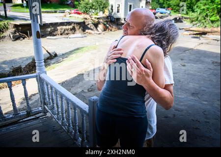 Plainfield, Vermont, Stati Uniti. 11 luglio 2024. Jim e Jenni Belotserkovsky si abbracciano dopo che la loro casa è stata inondata quando le piogge torrenziali dai resti dell'uragano Beryl hanno colpito il Vermont centrale, USA, il 10 luglio. Great Brook, un affluente del fiume Winooski, minò la casa in lontananza, che non è la loro casa ma la loro è vicina sul torrente. John Lazenby/Alamy Live News Foto Stock