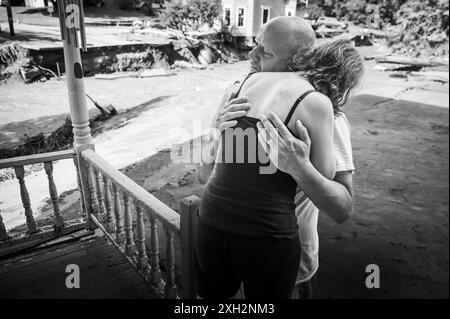 Plainfield, Vermont, Stati Uniti. 11 luglio 2024. Jim e Jenni Belotserkovsky si abbracciano dopo che la loro casa è stata inondata quando le piogge torrenziali dai resti dell'uragano Beryl hanno colpito il Vermont centrale, USA, il 10 luglio. Great Brook, un affluente del fiume Winooski, minò la casa in lontananza, che non è la loro casa ma la loro è vicina sul torrente. John Lazenby/Alamy Live News Foto Stock