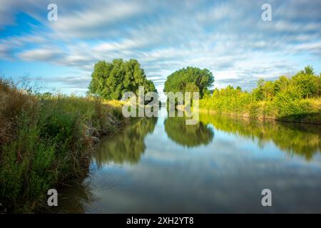 Splendido paesaggio del canale Castilla con alberi lungo il fiume ai suoi lati e il cielo riflesso nelle sue acque calme. Mentre passa attraverso Fromista, P. Foto Stock