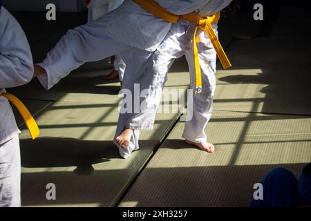 I bambini che praticano arti marziali in un dojo con cinture gialle e uniformi bianche Foto Stock