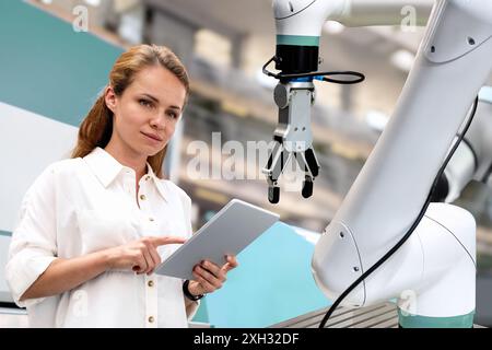 Giovane ingegnere donna in una startup di tecnologia robotica monitora da vicino le prestazioni di un braccio robotico autonomo in una produzione all'avanguardia Foto Stock