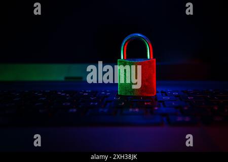 Un lucchetto verde e rosso si trova su una tastiera nera per laptop, illuminata da una luce blu morbida. Foto Stock