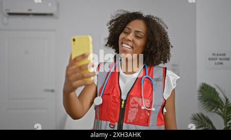 L'infermiera afroamericana sorride scattando selfie nel corridoio della clinica Foto Stock