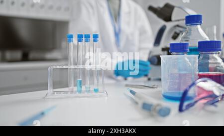 Uno scienziato attento che indossa un camice da laboratorio e guanti che conduce esperimenti in un laboratorio ben attrezzato Foto Stock