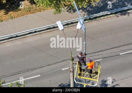 I lavoratori che installano su un sollevatore pneumatico per auto stanno installando una nuova lampada stradale. Foto Stock