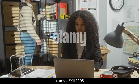 La detective donna analizza le informazioni sul portatile nella stazione di polizia con il suo collega maschio che cerca tra i file. Foto Stock