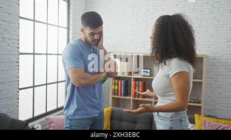 Una donna preoccupata parla con un uomo in difficoltà in un soggiorno moderno con libri e divano. Foto Stock