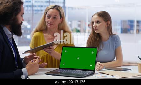 Clienti che cercano una guida personalizzata alla pianificazione su un notebook con schermo verde scritta dal consulente finanziario durante la riunione. Consulente che ottimizza le spese di vita per i clienti utilizzando il notebook mockup, la fotocamera B. Foto Stock