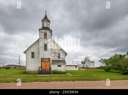 Vista esterna di una chiesa abbandonata e degli ascensori di grano distanti nel villaggio di Platone, Saskatchewan, Canada Foto Stock