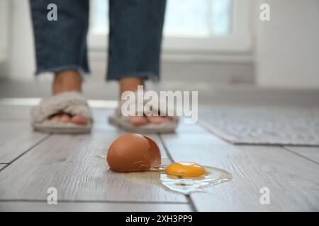 Donna vicina a un uovo crudo rotto su un pavimento in legno grigio in interni, messa a fuoco selettiva Foto Stock