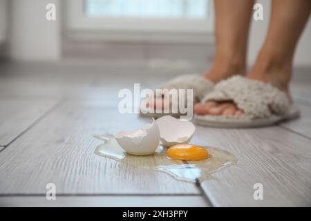 Donna vicina a un uovo crudo rotto su un pavimento in legno grigio in interni, messa a fuoco selettiva. Spazio per il testo Foto Stock