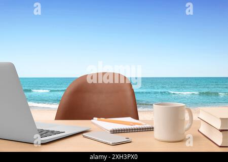 Posto di lavoro in spiaggia, ufficio lontano. Tavolo con laptop e sedia sulla spiaggia sabbiosa Foto Stock