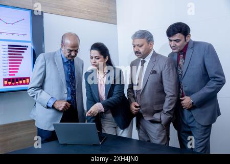 Uomo d'affari indiano senior con i suoi colleghi che parla della crescita aziendale con i notebook. finanza, analisi e concetto di luogo di lavoro. Foto Stock