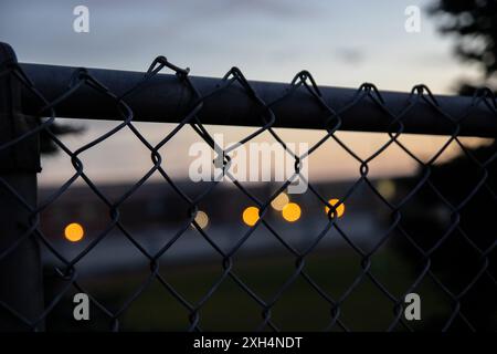 Luci bokeh al tramonto dietro la recinzione a catena - sfondo urbano sfocato con calde sfere luminose - gradiente del cielo al crepuscolo. Presa a Toronto, Canada. Foto Stock