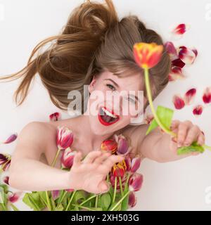 La bella signora si mette in posa con i tulipani per il giorno della donna, con fiori incastonati sul petto e nelle mani. Espressione sorridente donna bionda beamin Foto Stock