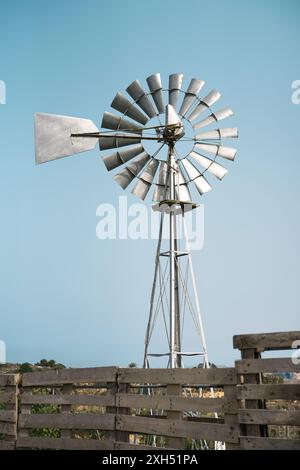 Rustico mulino a vento in piedi alto con un cielo azzurro limpido sullo sfondo. Fotografato in una giornata di sole, cattura una tranquilla scena rurale. Foto Stock