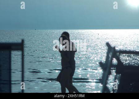 Una persona che cammina su una spiaggia nebbiosa, circondata da nebbia e onde oceaniche, Una figura solitaria che cammina lungo la costa, persa nel pensiero Foto Stock